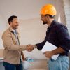 Happy worker and his clients shaking hands at constriction site. Copy space.